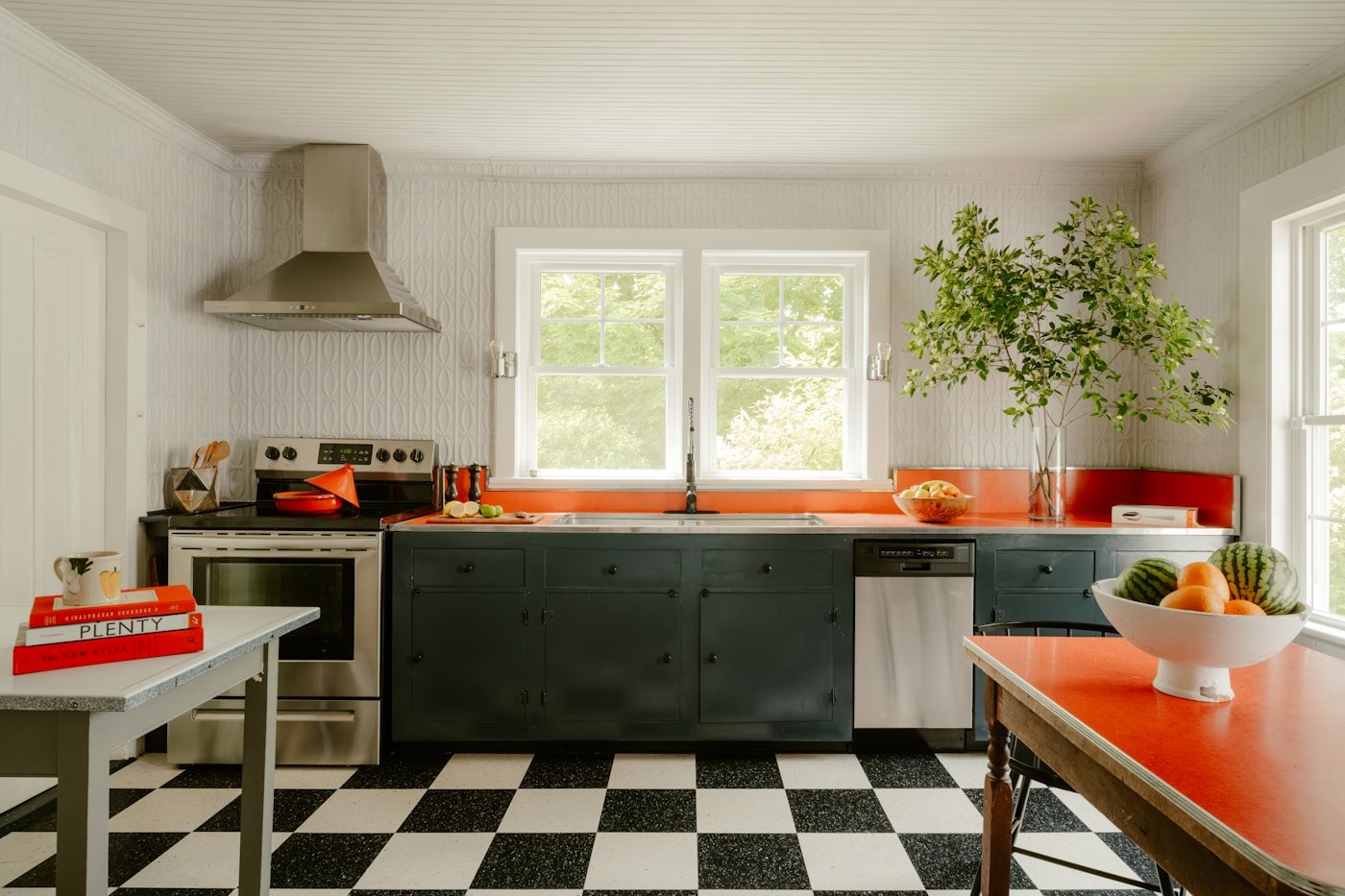 A bright kitchen with a checkerboard floor and dark green cabinets