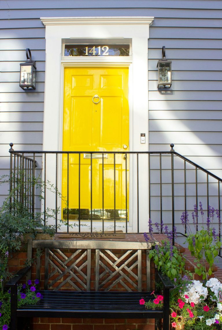 A welcoming porch with a bright yellow front door, white trim, and a bench with flowers