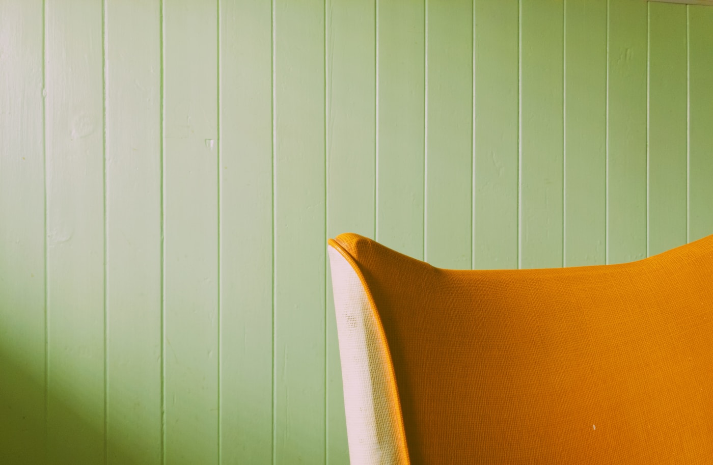 Bright orange chair against a fresh green paneled wall