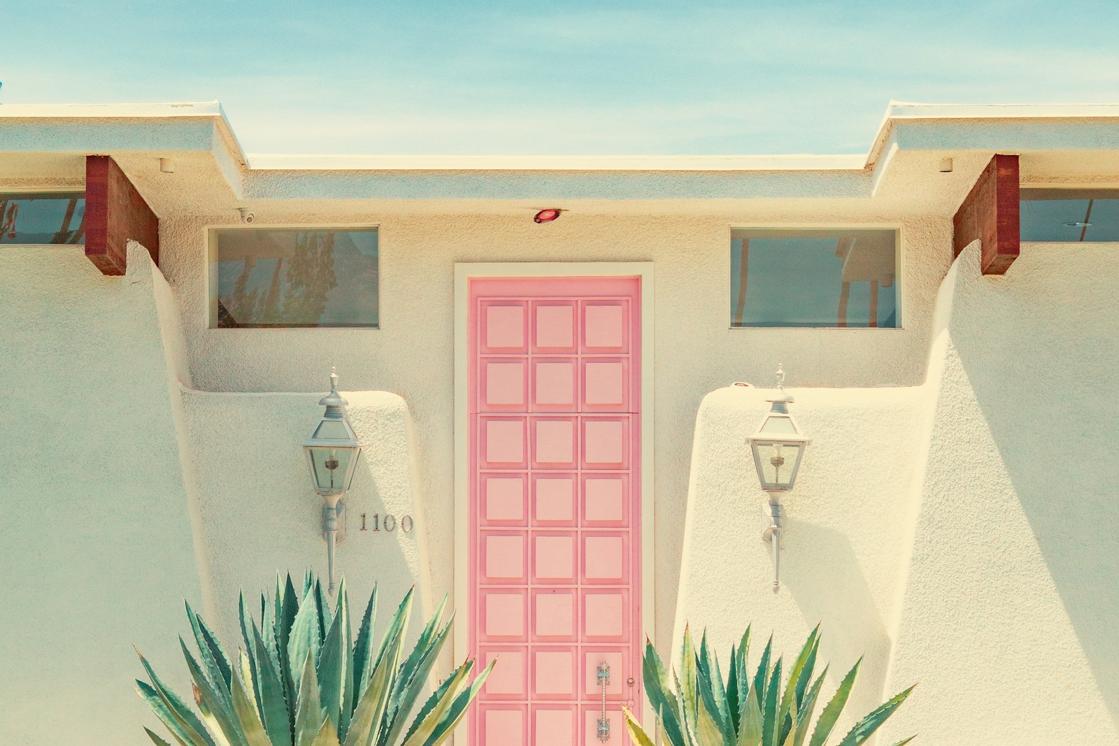 Bright pink front door framed by green plants on a white house