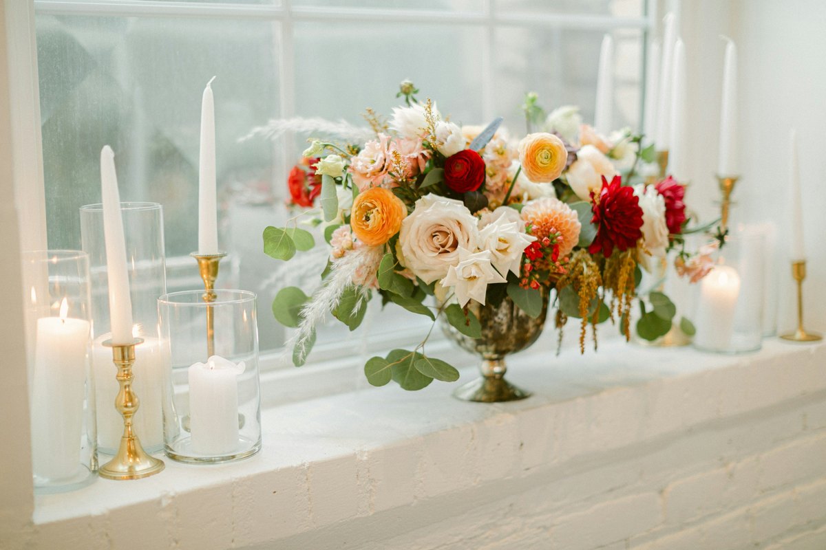 A floral arrangement with lit candles on a windowsill