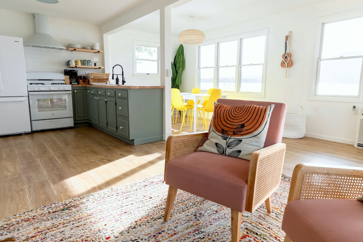 A cheerful living room with green cabinets, warm chairs and yellow stools