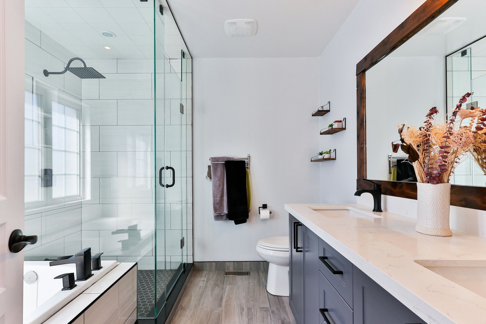 A clean white bathroom with a glass shower, black fixtures and a clear vanity counter