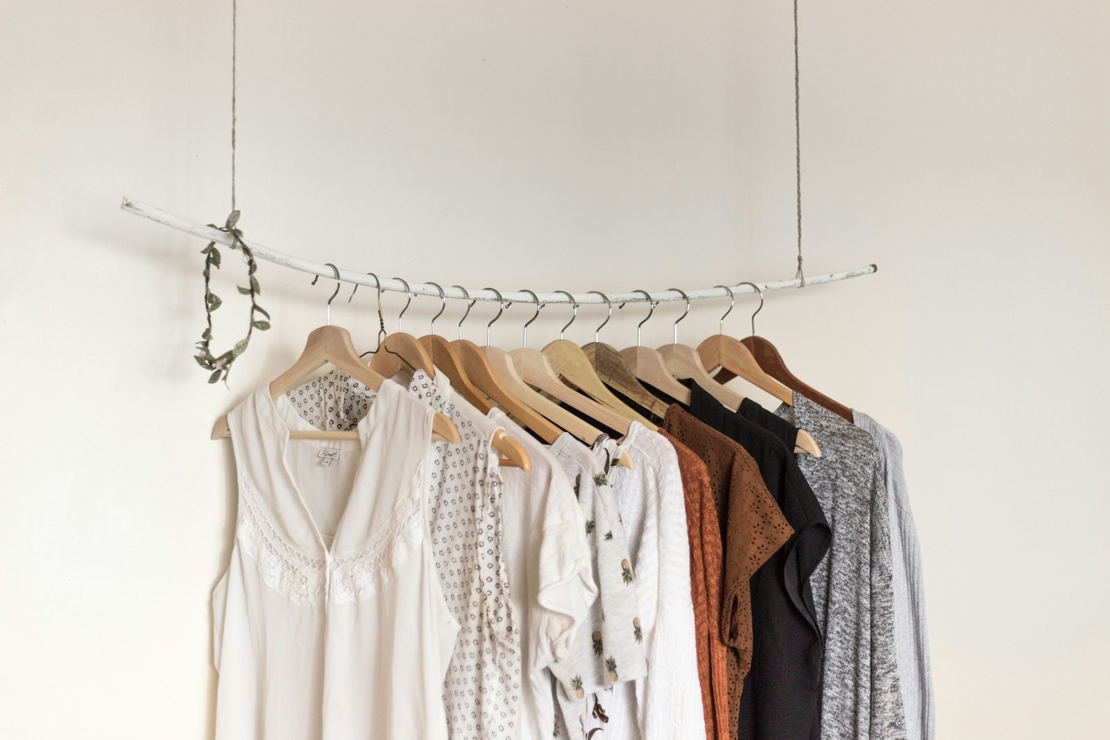 A half-empty clothes rail with a few blouses on matching wooden hangers against a white wall