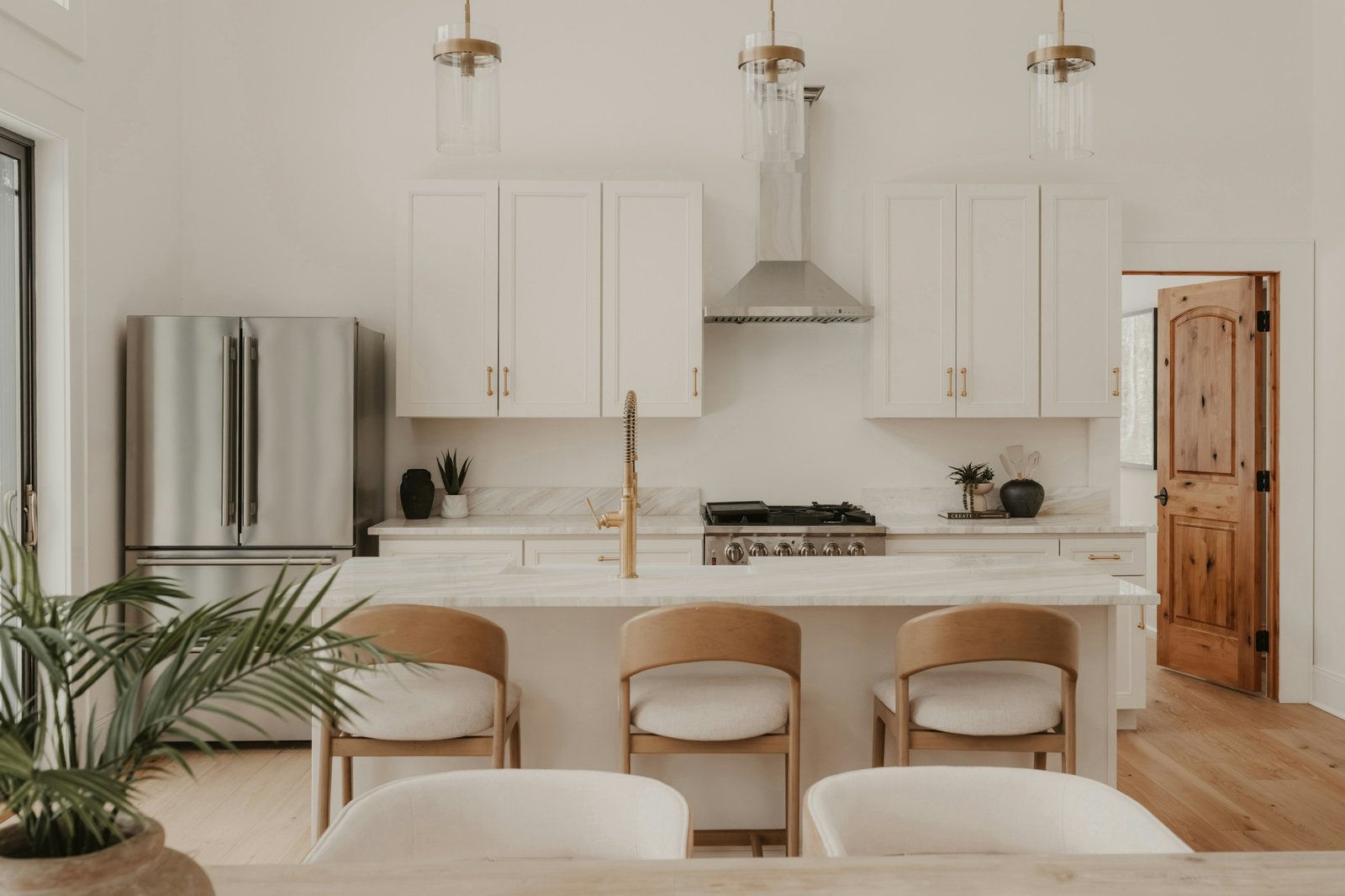A bright white kitchen with clear marble counters, brass hardware and three stools at the island