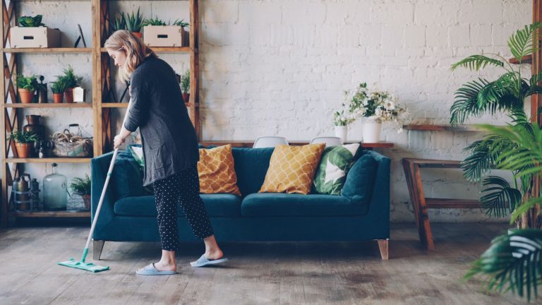 A woman mopping a colorful living room with a teal sofa and yellow cushions