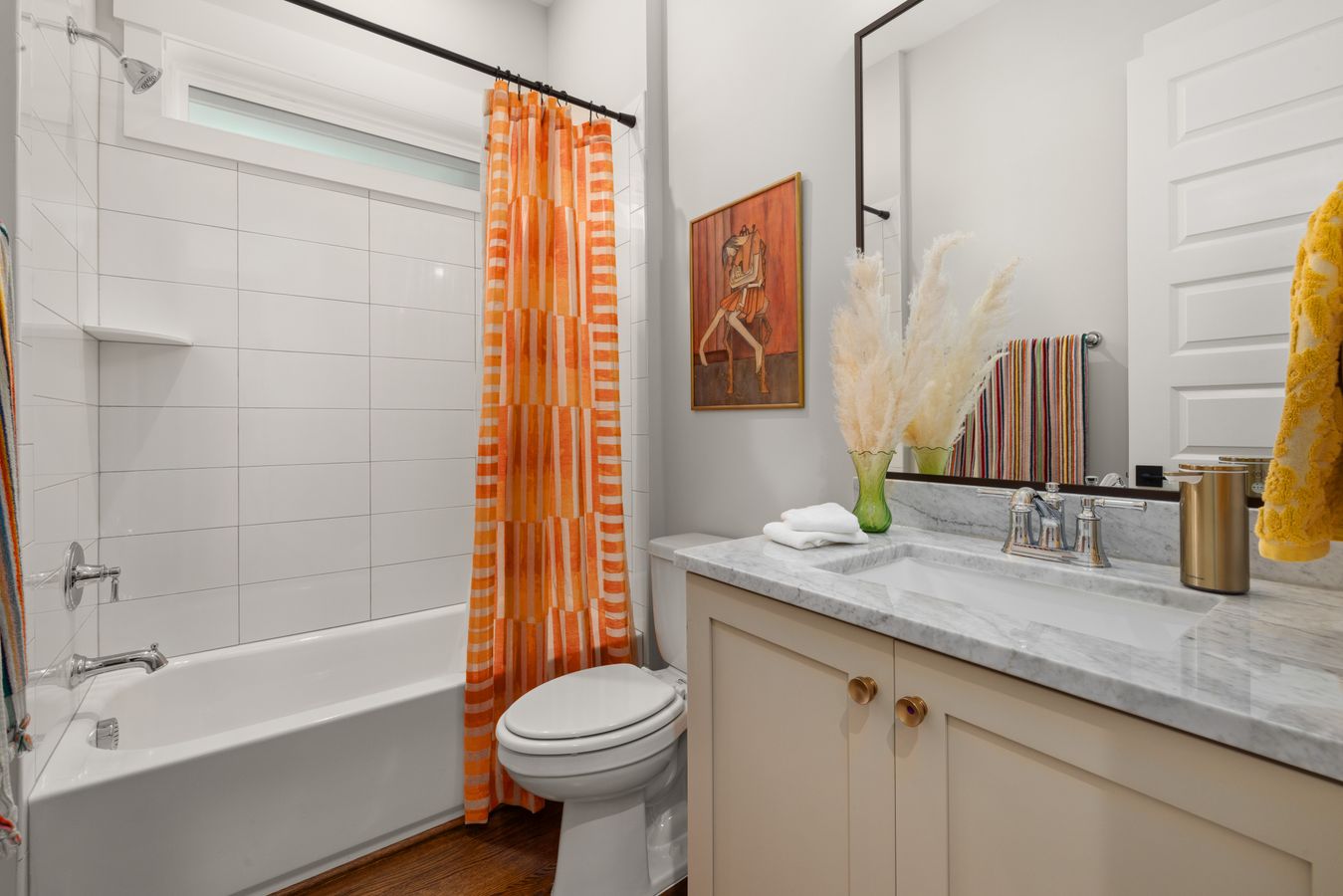 A bright bathroom with an orange striped shower curtain and colorful towels