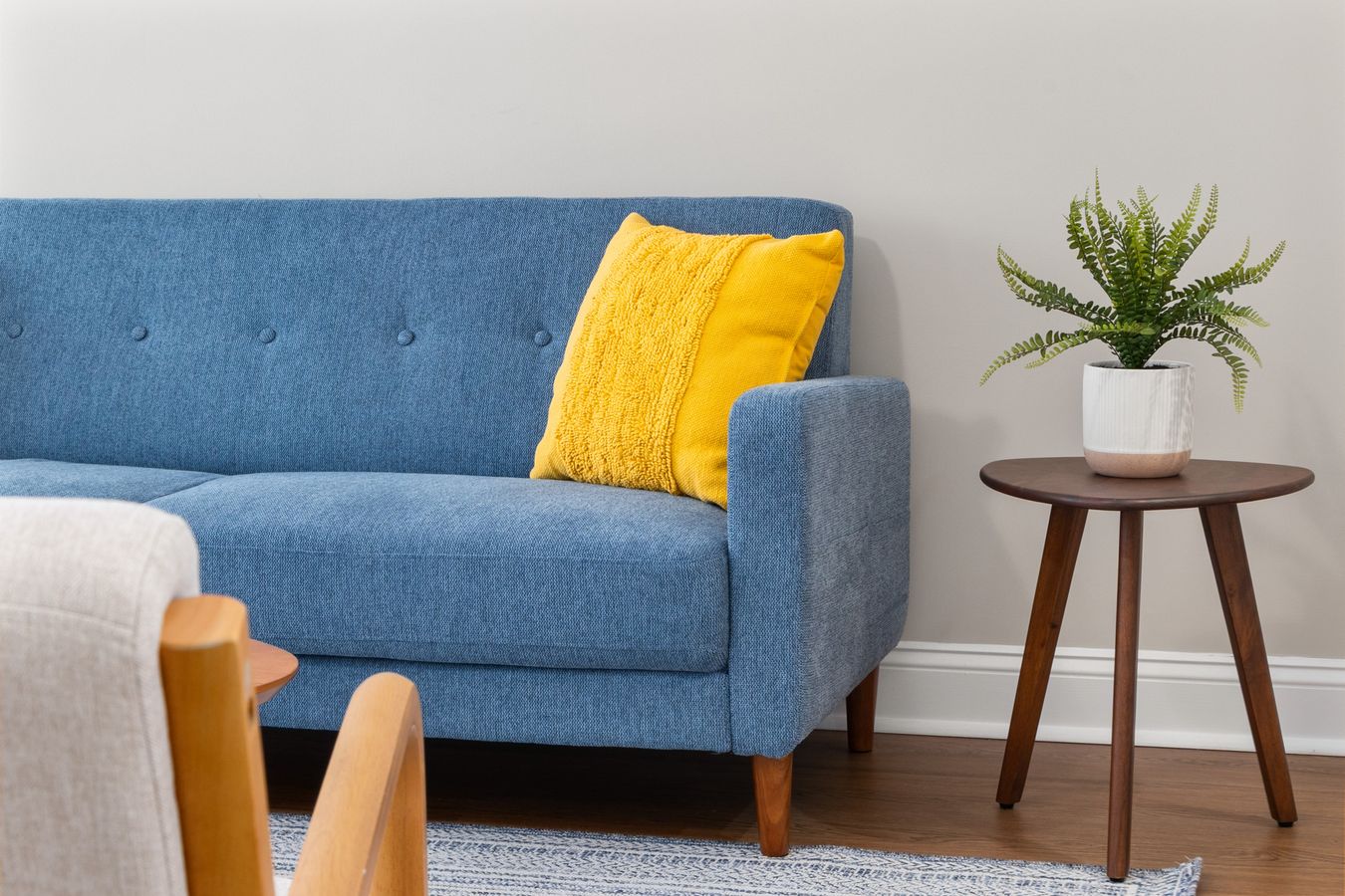 A blue sofa with a yellow cushion and a wooden side table within easy reach