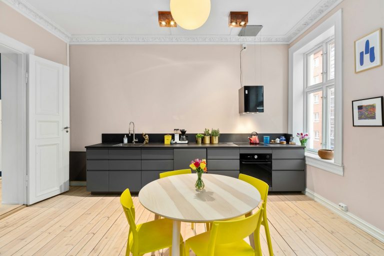 A bright kitchen with yellow dining chairs, dark cabinets, flowers and colorful accents
