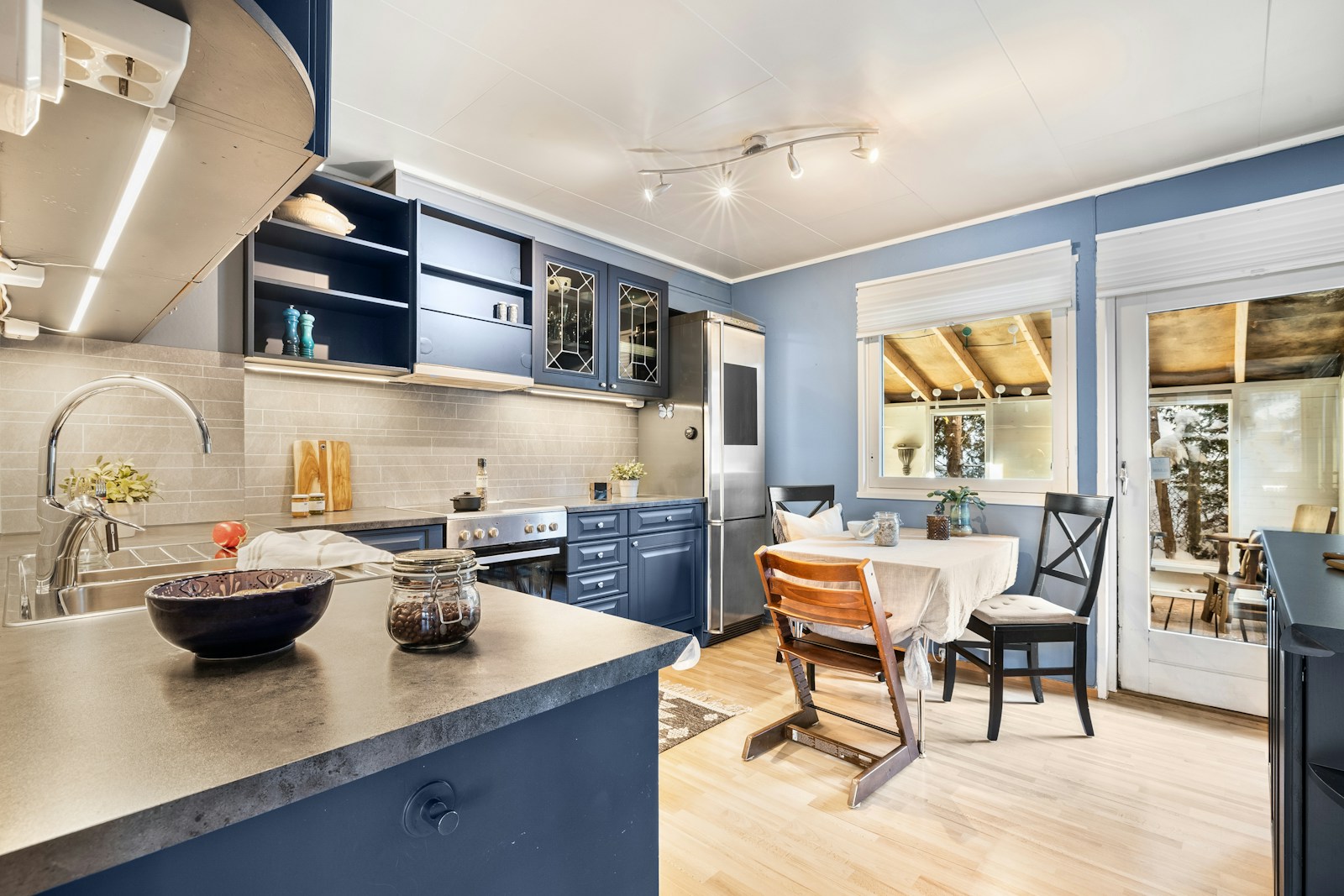 A bright kitchen with blue cabinets, clear worktops, a small dining table and light wood flooring