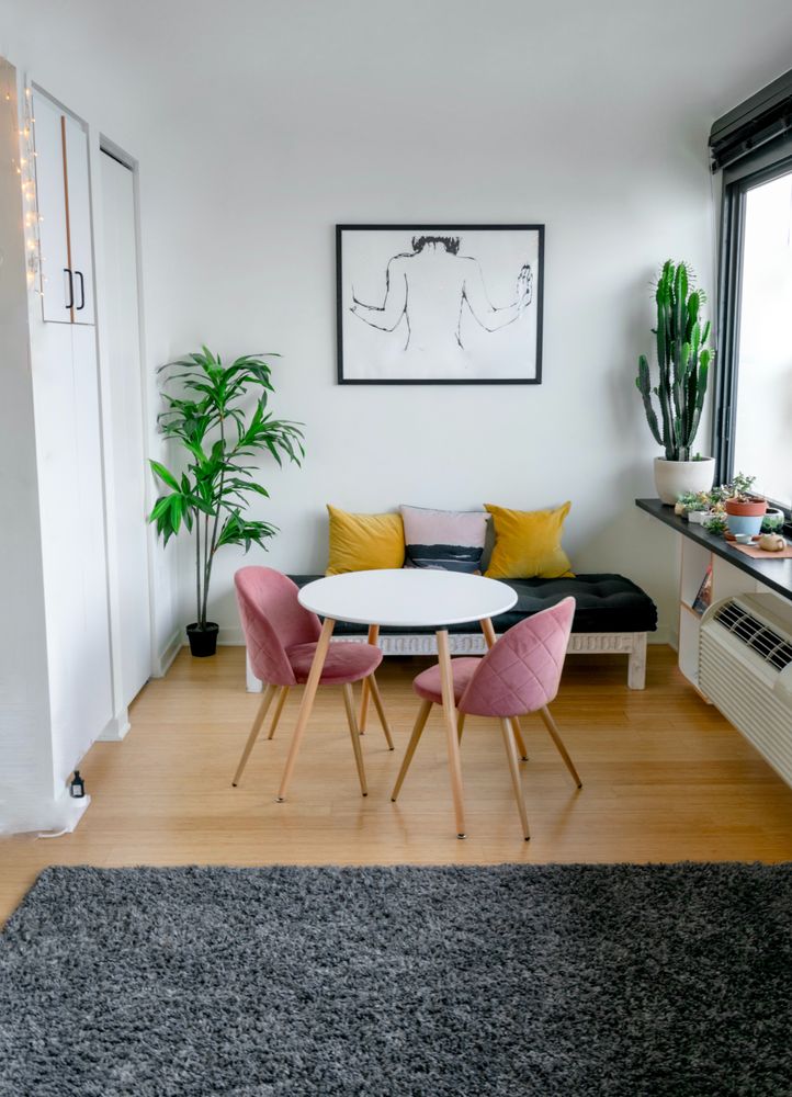 A bright dining nook with pink chairs, mustard-yellow cushions, plants and a round white table