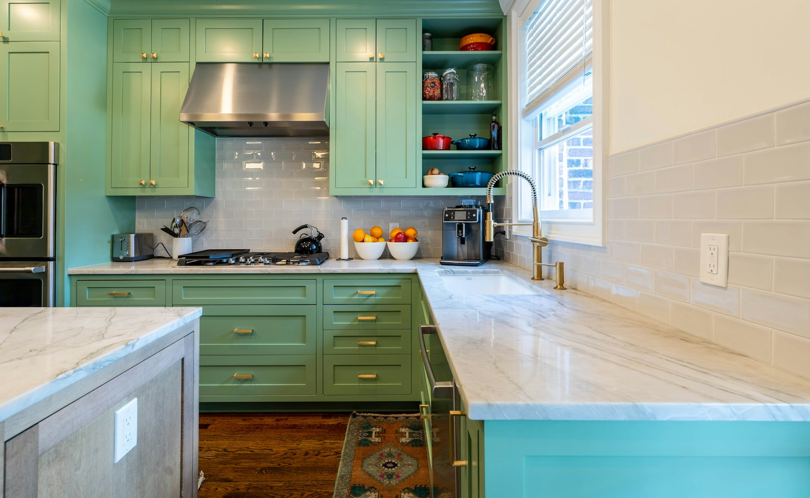 Bright kitchen with green cabinets, brass handles and light stone counters