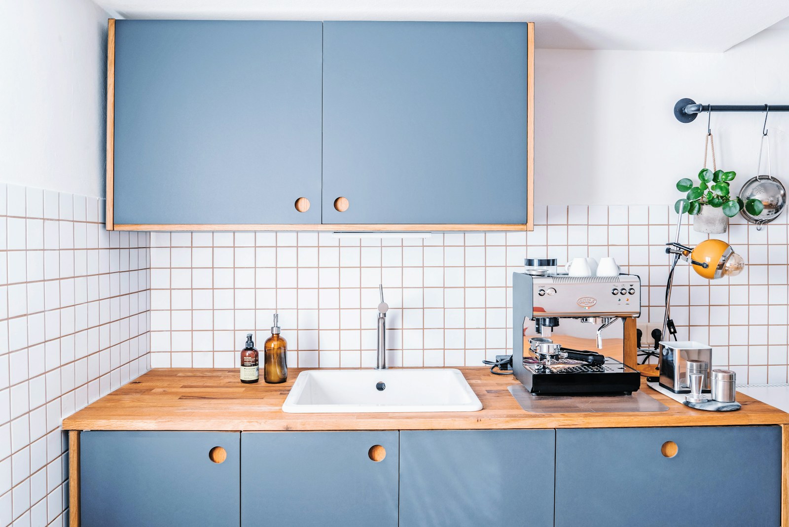 Blue kitchen cabinets with round wooden knobs, a white sink and a clear wooden counter