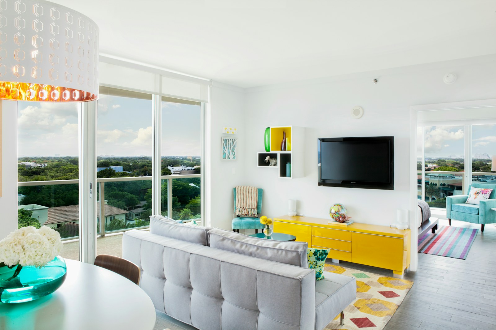 Sunlit living room with yellow storage, turquoise accents, a gray sofa and large windows