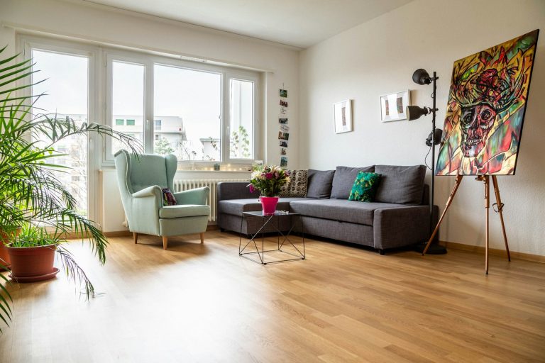 Bright living room with a green armchair, gray sofa, colorful painting and large windows