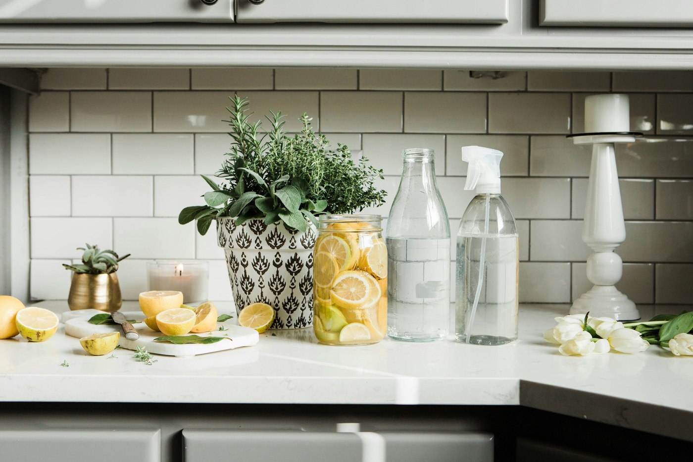 Lemons, glass bottles and green plants arranged on a bright kitchen counter