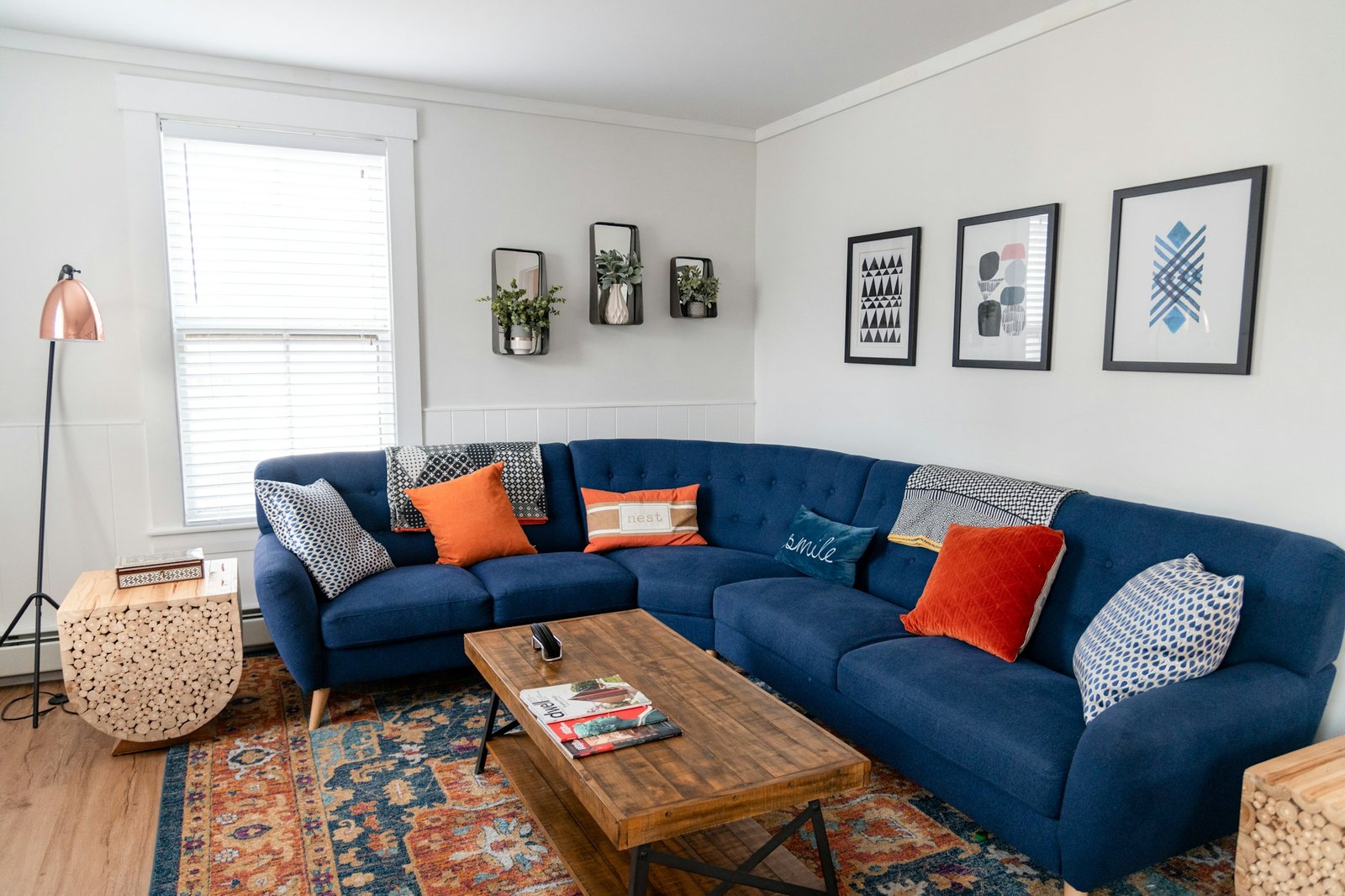 A bright living room with a blue sectional sofa, orange pillows and framed art
