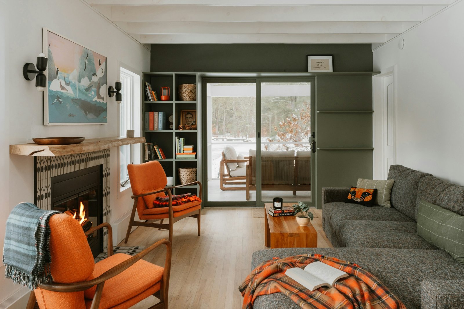 A cozy living room with a fireplace, two orange armchairs and a gray sectional