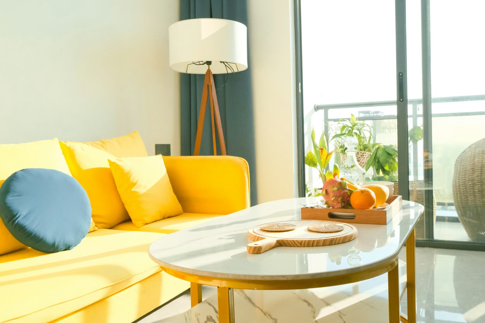 A sunny condo living room with a yellow sofa and a round white table by the balcony doors