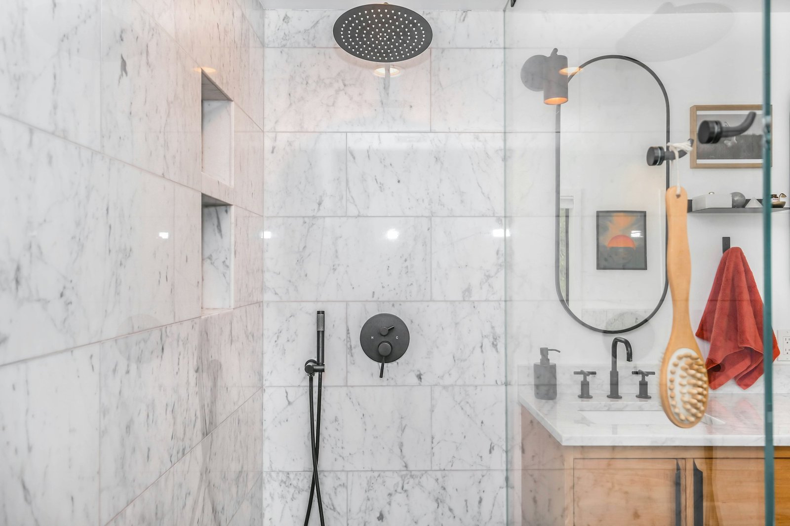 A curbless walk-in shower with marble tile, a handheld showerhead and a glass panel