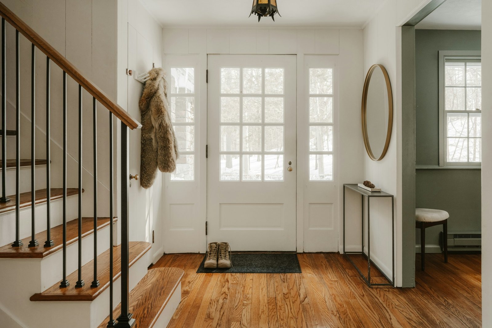 A white entryway with a glass front door, wood floors and a staircase