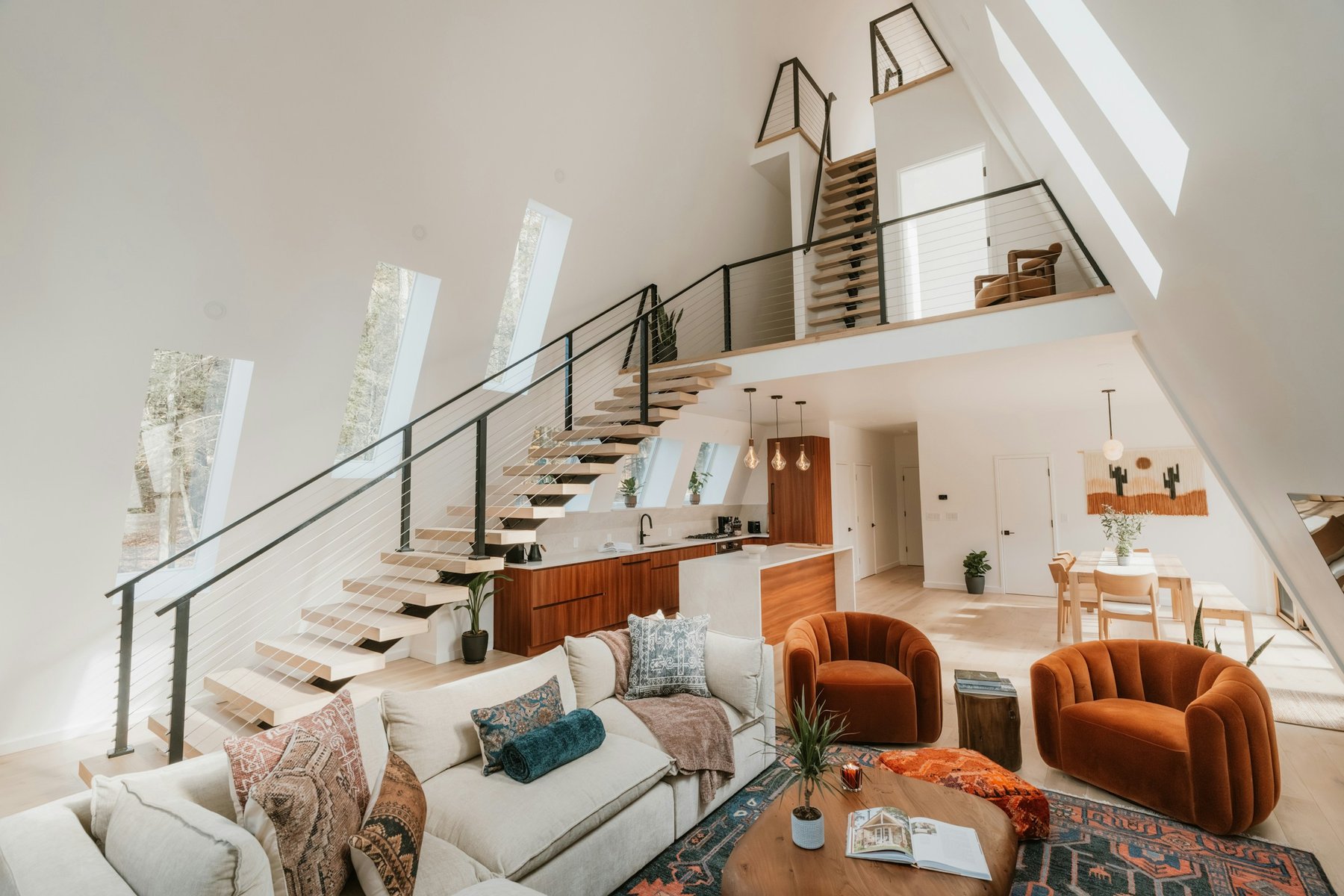 A bright modern living room with an open staircase to a loft and two orange armchairs