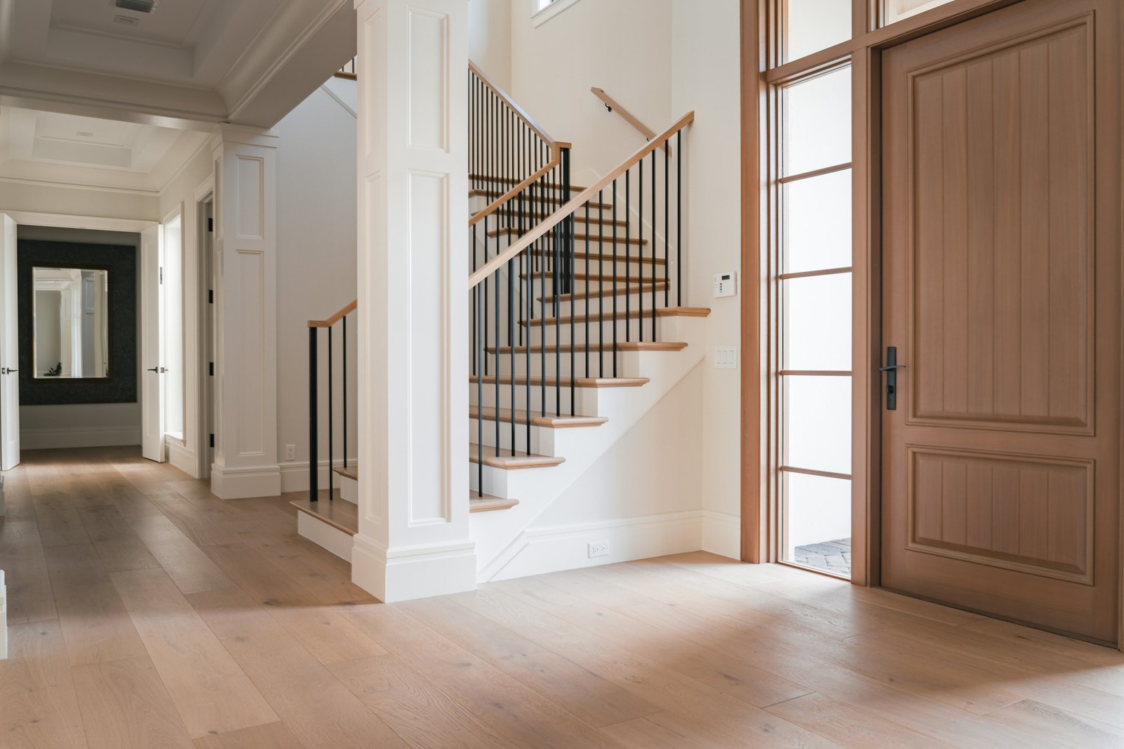 A bright white foyer with a wooden staircase, iron balusters and a wide front door