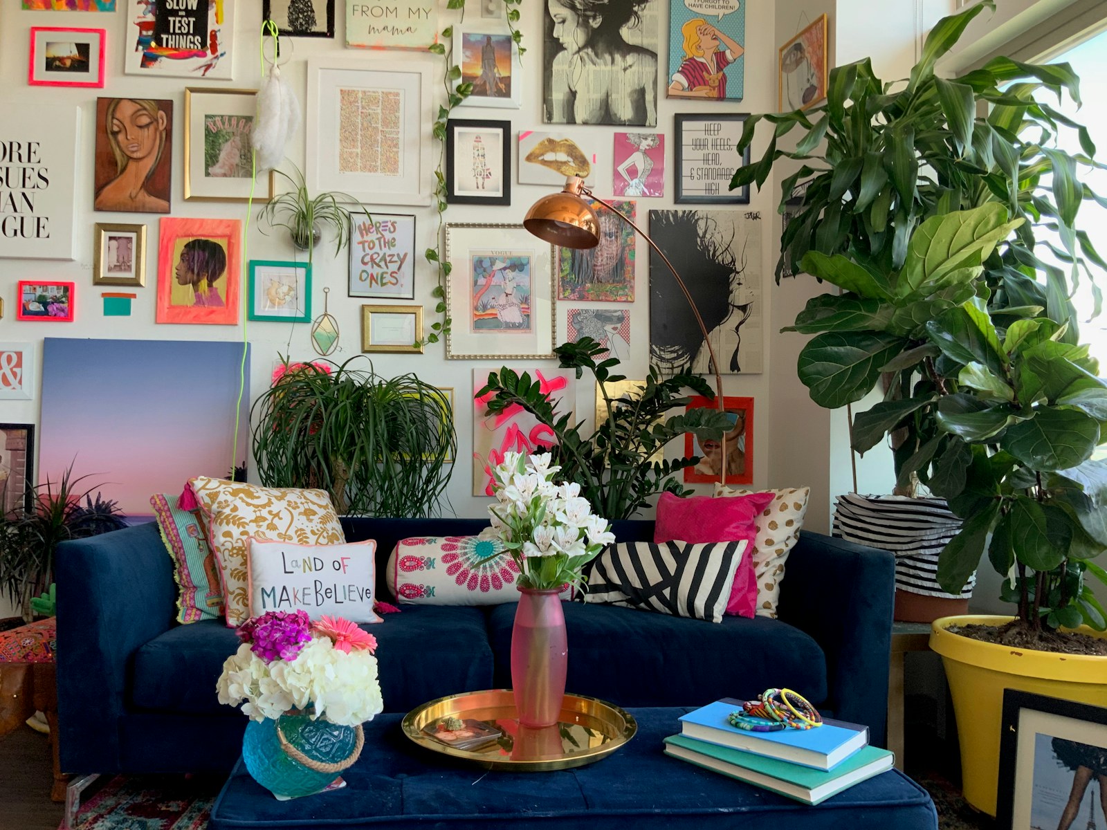 Gallery wall of colorful art above a navy sofa with patterned pillows and plants