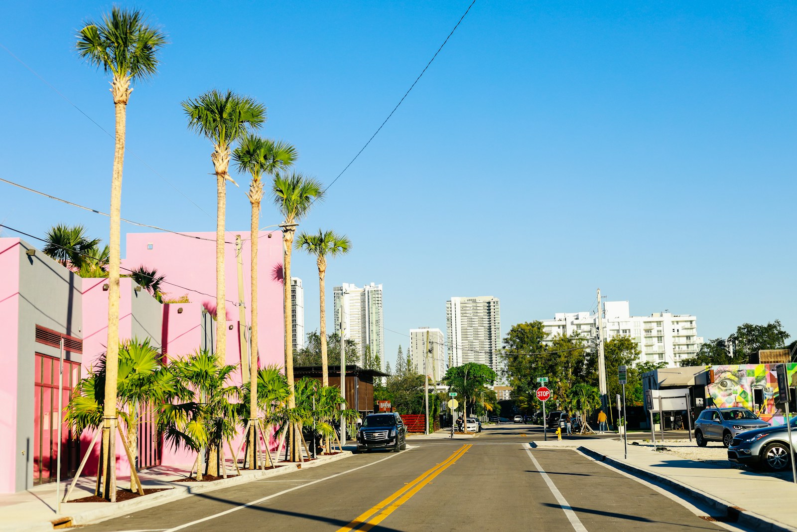 Pink and coral buildings along a palm-lined street under a blue sky