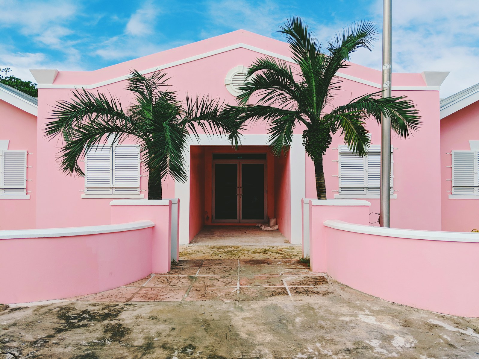 Pink stucco house with palm trees and a white garden wall under a bright sky