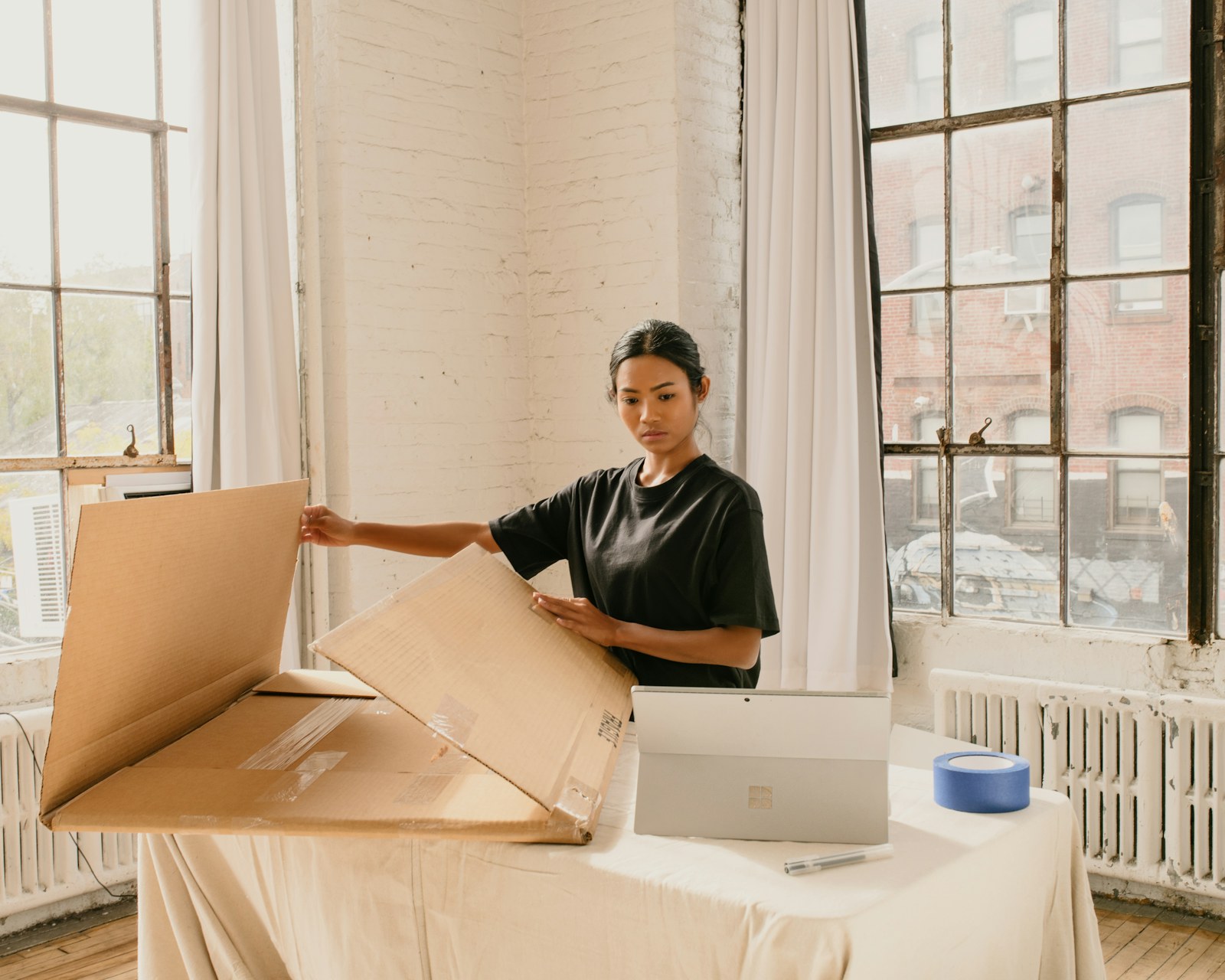 A woman folding a cardboard box on a table in a bright white loft apartment