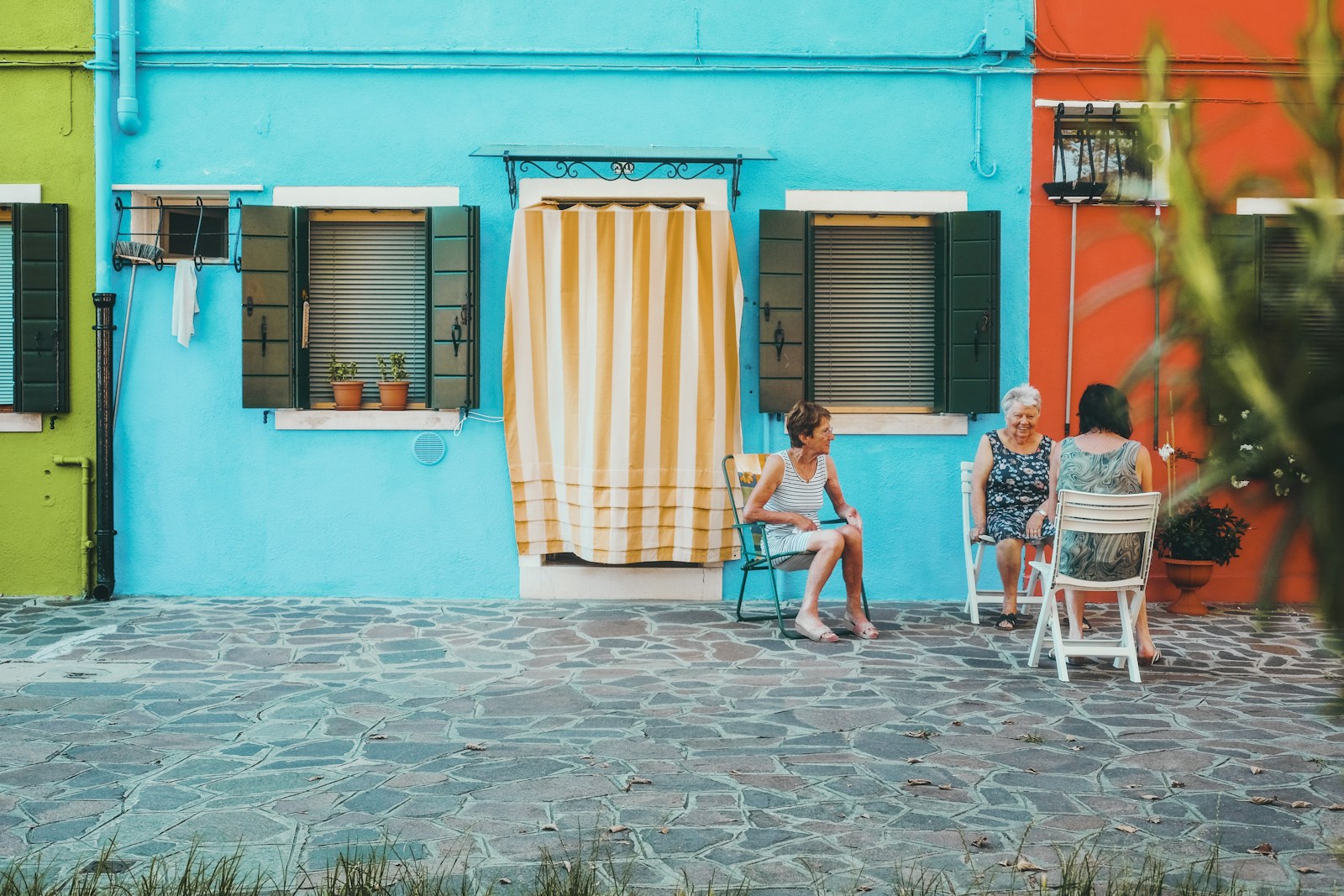 Neighbors sitting outside a turquoise and teal house on a sunny lane